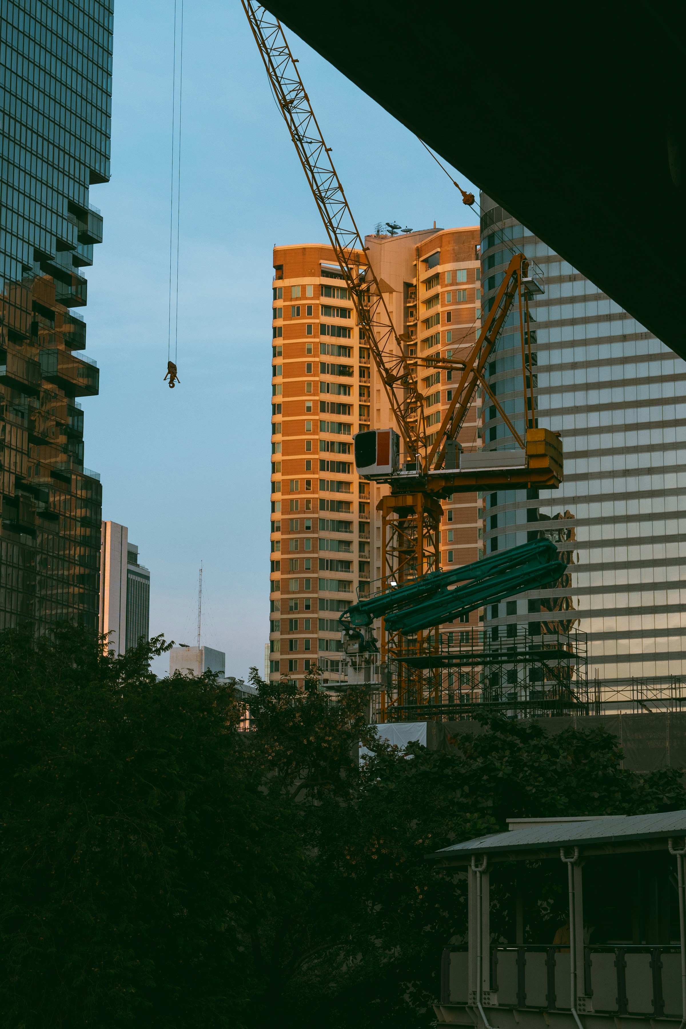 Construction crane amidst tall urban buildings during early evening under clear sky.